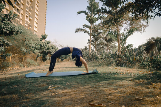 Woman doing Urdhva Dhanurasana yoga (Wheel Pose or Upward Bow Pose) in the garden. International Yoga Day