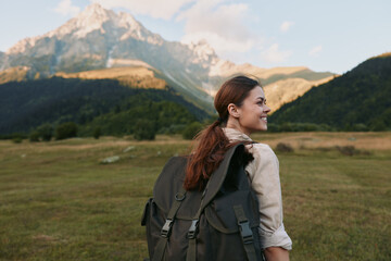 Fototapeta premium Cheerful woman outdoors, smiling over her shoulder, hiking with a backpack, mountains and valley in warm sunlit light, natural lifestyle moment