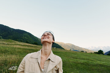 Fototapeta premium A young woman in a beige jacket tilts her head back and smiles in a sunlit meadow under a clear sky, capturing a moment of lighthearted outdoor freedom and contentment.