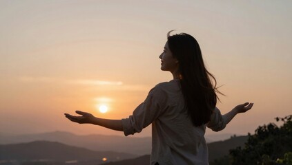 Fototapeta premium Woman stands with outstretched arms watching the sunset over the hills