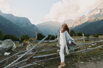 Fototapeta premium Cheerful woman outdoors, enjoying mountains, scenery, casual outfit, flowing cardigan, sunlit air, relaxed pose, natural colors, alpine landscape, carefree mood