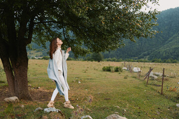 Obraz premium Woman enjoying outdoors under a leafy tree, casual lifestyle moment, breeze in hair, field and mountains in the background, natural serene colors