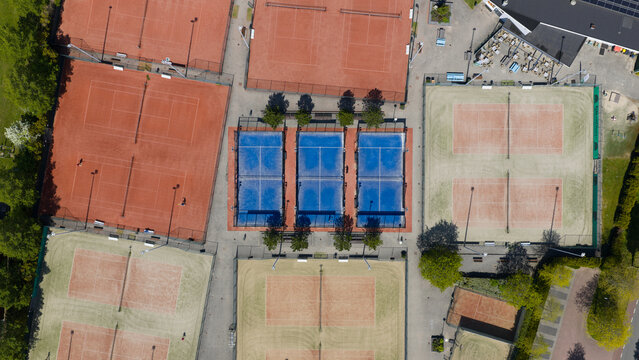 Aerial view of Tennis Padel Club Heiloo featuring red clay tennis courts and blue padel courts surrounded by lush green trees in Heiloo, Noord-Holland, Netherlands.