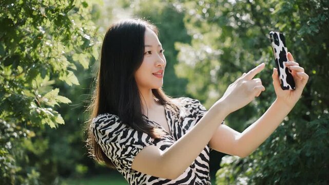 Young Asian Woman Taking Selfies with a Smartphone in a Sunny Park