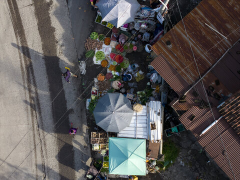 Aerial view of Pasar Kembang Klaten traditional market with colorful vegetable stalls, umbrellas, and people walking on the street next to rusty rooftops Klaten, Central Java, Indonesia.