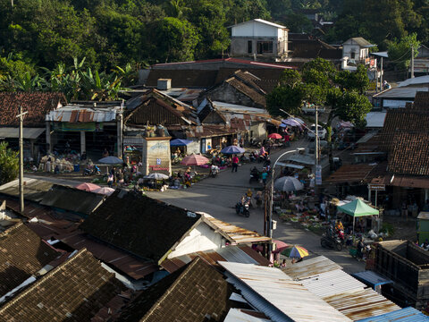 Aerial view of the bustling Pasar Kembang Klaten traditional market with people, stalls, and motorcycles among historic rooftops and lush greenery in Klaten, Central Java, Indonesia.