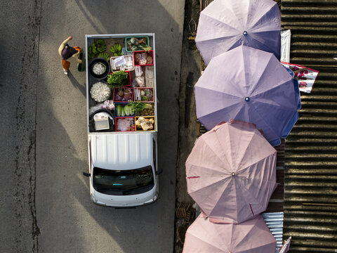Aerial view of a white truck filled with fresh vegetables parked beside colorful market umbrellas at Pasar Kembang Klaten in Klaten, Central Java, Indonesia.