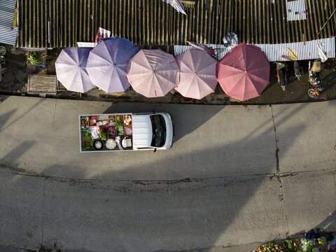 Aerial view of Pasar Kembang Klaten traditional market with a white pickup truck carrying fresh vegetables on the road next to colorful umbrellas at Klaten, Central Java, Indonesia.