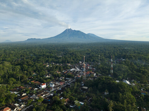 Aerial view of Pasar Kembang Klaten traditional market and village houses surrounded by dense tropical forest with Mount Merapi volcano in the background Klaten, Central Java, Indonesia.