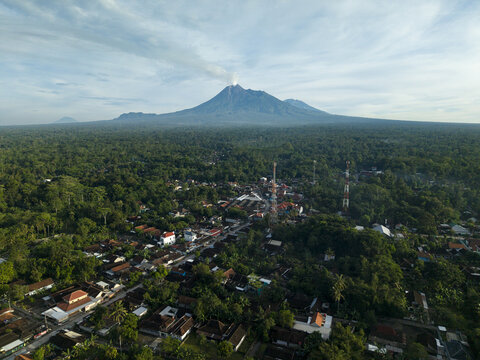 Aerial view of the village featuring Pasar Kembang Klaten traditional market and the smoking Mount Merapi volcano in the background Klaten, Central Java, Indonesia.