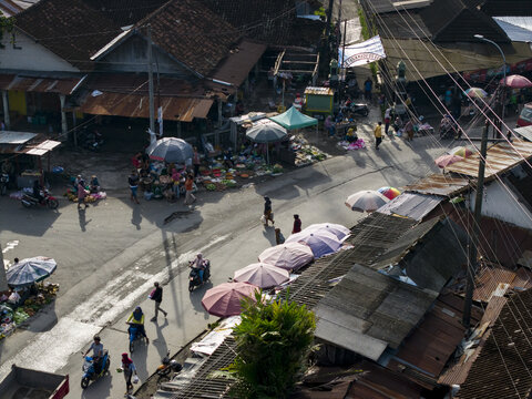 Aerial view of Pasar Kembang Klaten traditional market with people on motorbikes, colorful umbrellas, and rustic rooftops in Klaten, Central Java, Indonesia.