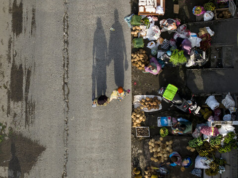 Aerial view of Pasar Kembang Klaten traditional market with people walking on the road and vendors selling fresh produce on the roadside in Klaten, Central Java, Indonesia.