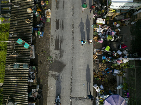 Aerial view of Pasar Kembang Klaten traditional market with people walking on the road and stalls under corrugated roofs in Klaten, Central Java, Indonesia.