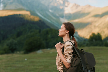 Fototapeta premium Cheerful woman outdoors, hiking through a sunlit meadow with distant mountains, wearing a backpack, relaxed smile, natural colors, lifestyle moment, calm breeze