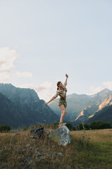 Fototapeta premium Young woman balances on a rock in a mountain meadow, enjoying fresh air and freedom.