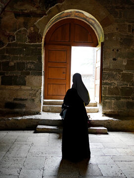 A rear view of a woman in a black clothing and headscarf standing before an open wooden doorway in Trabzon, Turkey