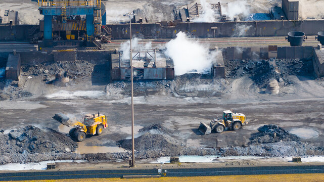 Aerial view of the Tata Steel industrial site with wheel loaders operating near piles of raw materials and rising steam in Velsen-Noord, Noord-Holland, Netherlands.