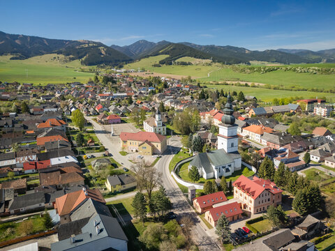 Aerial view of the historic village featuring St. Matthew's Church, traditional red-roofed houses, and rolling green hills under a clear sky Partizanska Lupca, Zilina Region, Slovakia.