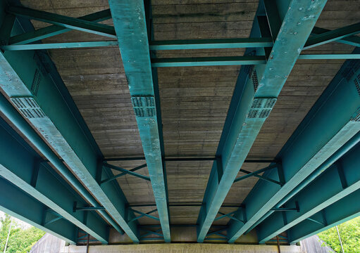 The underside of a plate girder bridge with turquoise I-beams, England, UK