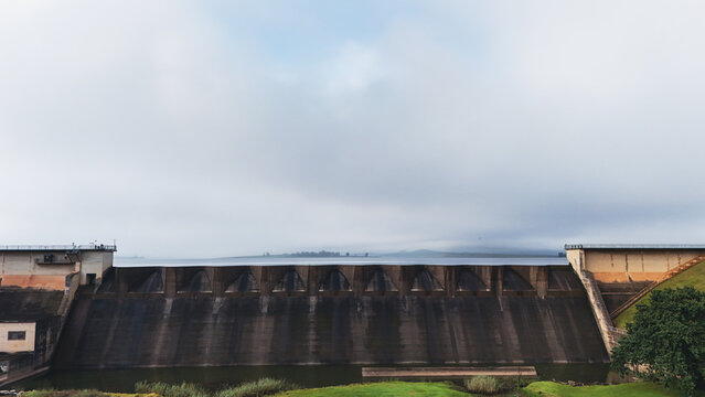 Aerial view of the massive concrete spillway of Midmar Dam with calm water and misty hills under an overcast sky in Howick, KwaZulu-Natal, South Africa.