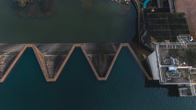 Aerial view of the Midmar Dam featuring its unique zigzag spillway and concrete infrastructure over dark water in Howick, KwaZulu-Natal, South Africa.