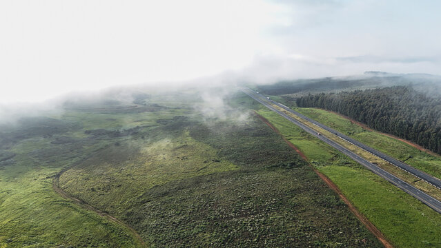 Aerial view of a highway cutting through green hills and forests partially covered by low clouds Garden Route District Municipality, Western Cape, South Africa.