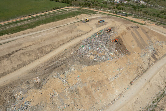 Brasov, Romania - 28 April 2026: Aerial view of a large landfill site with heavy machinery, excavators, and trucks managing waste piles under a clear sky.