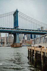 Fototapeta premium View of Manhattan Bridge tower from East River wooden pier. Steel suspension tower of Manhattan Bridge seen from a weathered wooden dock on the riverfront.