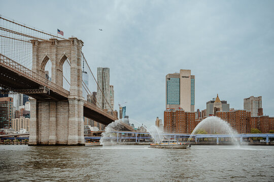New York, USA, 2 May 2026: FDNY fireboat spraying water salute near Brooklyn Bridge in New York. Fireboat performing water display on East River with Brooklyn Bridge and Manhattan skyline background.