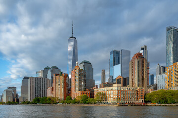 Obraz premium Lower Manhattan skyline and One World Trade Center from river. Panoramic view of skyscrapers and One World Trade Center in New York City from the Hudson River under cloudy sky.