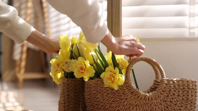 Woman arranging beautiful flowers in wicker bag indoors, closeup