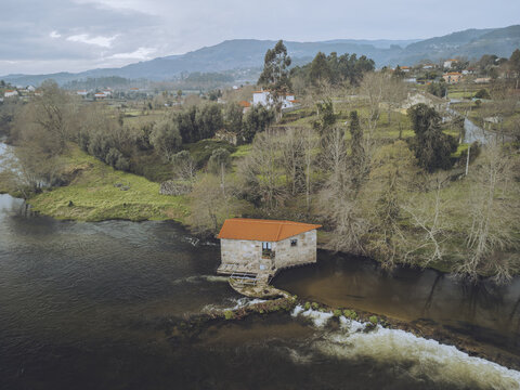 Aerial view of watermill house by the serene Lima River surrounded by tranquil hills and lush trees, Jolda, Viana do Castelo, Portugal.