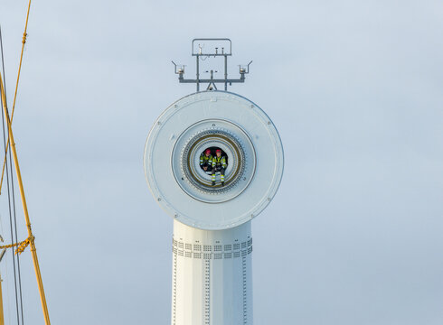Netherlands - 26 November 2025: Aerial view of two technicians in high-visibility clothing sitting inside the nacelle of a large offshore wind turbine against a clear sky.