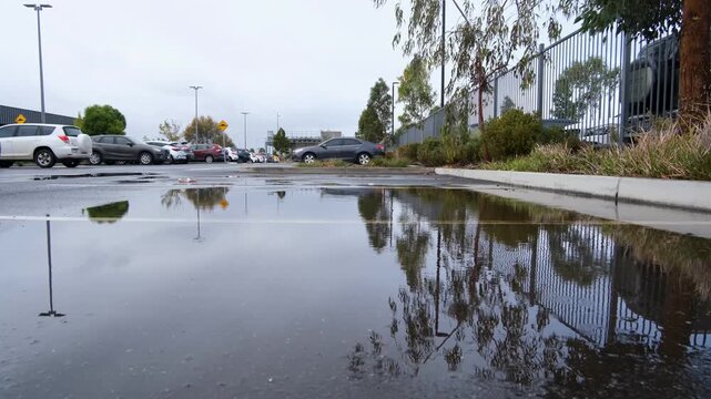 Water pooling and flooding in a suburban public car park in Melbourne, Australia, after heavy rain, with reflections of parked cars in the standing water. Poor drainage and stormwater management 