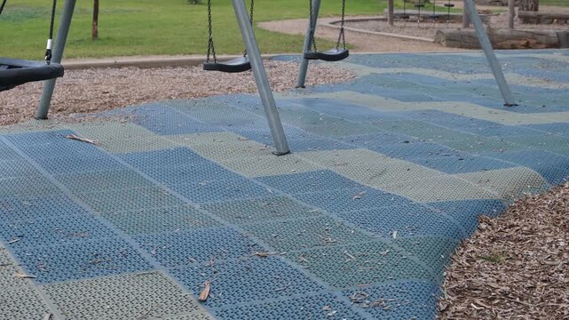 Rubber safety matting beneath a swing set in a suburban playground in Melbourne,  Australia, with wood chip mulch surrounding impact-absorbing surface. Safety standards and child-friendly design