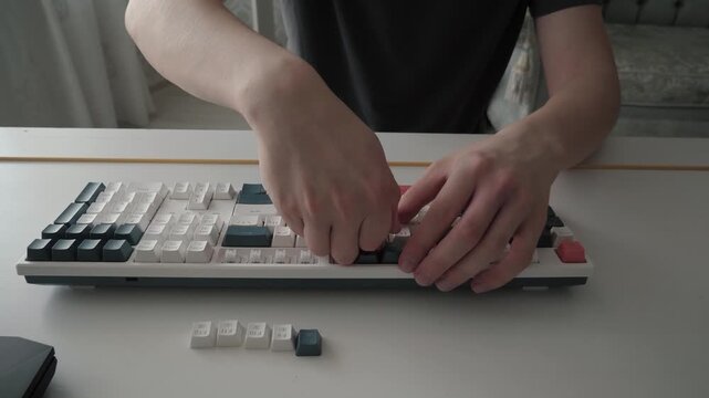 Hands modifying keyboard. Close up of hands customizing mechanical keyboard with precise movements. Person using tool to replace and align keys on minimalistic workspace in soft natural lighting
