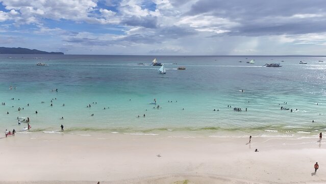 Malay, Philippines - 02 May 2026: Aerial view of Boracay Island featuring turquoise waters, white sand beach with people swimming, and traditional sailboats under a cloudy sky.