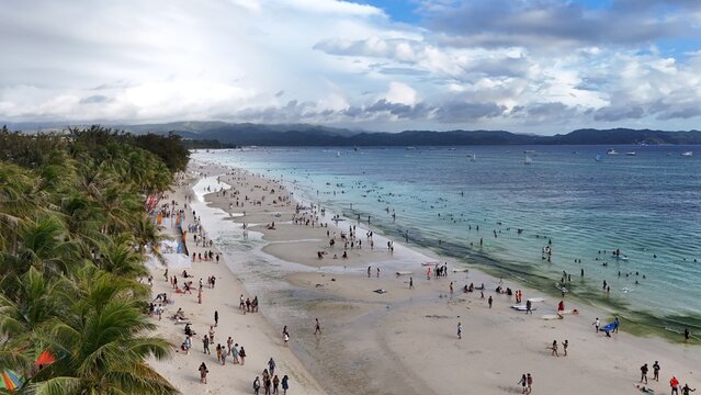 Malay, Philippines - 02 May 2026: Aerial view of Boracay Island featuring white sand, turquoise waters, and crowds of people under a cloudy sky.