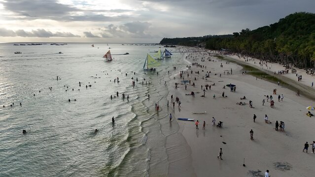 Malay, Philippines - 02 May 2026: Aerial view of Boracay Island featuring the crowded white sand beach with sailboats and people swimming under a cloudy sky.