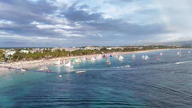 Malay, Philippines - 02 May 2026: Aerial view of Boracay Island featuring numerous traditional sailboats on turquoise waters along the sandy coastline lined with palm trees and resorts.