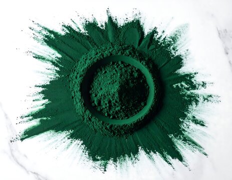 Symmetrical spirulina powder blast on white marble surface, artistic green pigment burst for health and beauty.