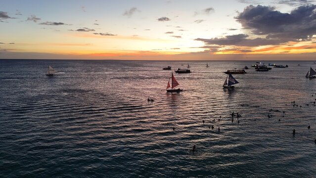 Malay, Philippines - 02 May 2026: Aerial view of Boracay Island featuring traditional sailboats on the calm sea and people swimming during a vibrant sunset.