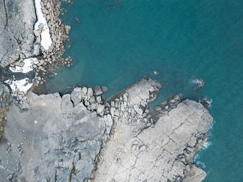 Svalbard and Jan Mayen - 28 July 2025: Aerial view of the rugged rocky coastline with fractured stone formations and turquoise arctic waters.