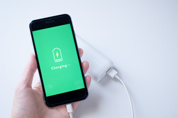 白いモバイルバッテリーに接続して充電中のスマートフォン（画面デザインはオリジナル制作） © Keyglad