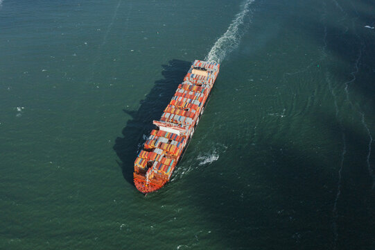 05 September 2019: Aerial view of a massive container ship transporting colorful cargo across the open ocean with a prominent white wake.