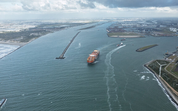 Rotterdam, Netherlands - 05 September 2019: Aerial view of a large container ship navigating through a canal towards the industrial port area under a cloudy sky.