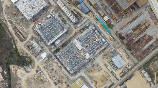 Tambon Khlong Tamru, Thailand - 11 March 2026: Aerial view of a large industrial construction site with multiple buildings under development, yellow cranes, and organized building materials.