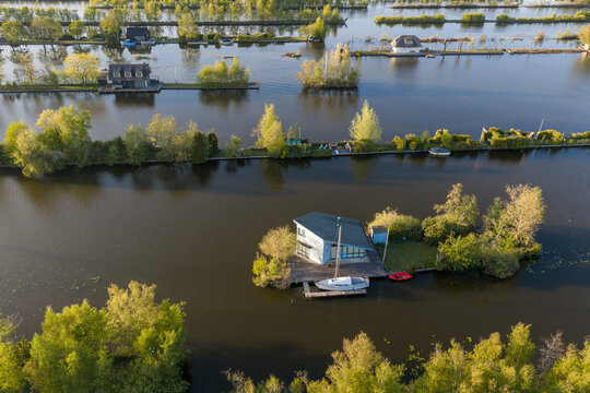 Breukelen, Netherlands - 25 April 2026: Aerial view of Scheendijk recreational islands with small houses, lush green trees, and boats on the calm water.
