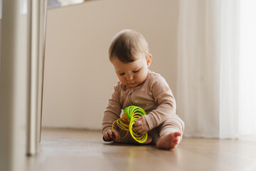 Fototapeta premium A young child plays with an educational toy. The sun is shining through a window, creating a warm atmosphere. Concept of teething period, baby care, early development, and healthy childhood life