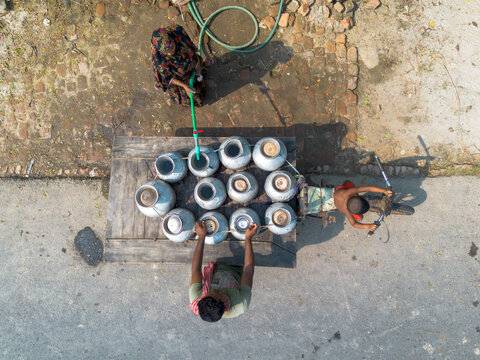 Satkhira, Bangladesh - 20 April 2026: Aerial view of people filling metal water jugs on a wooden cart with a hose on a sunny day.